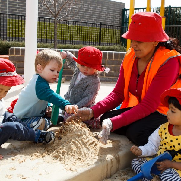 educator playing in sandpit with 4 toddlers