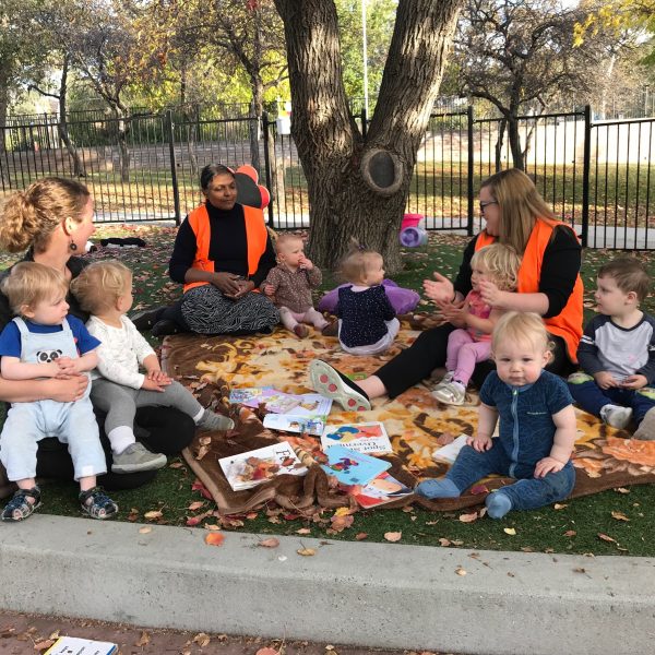 children sitting with educators in park reading books