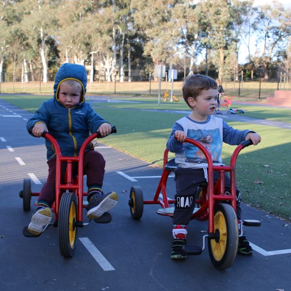 two preschoolers riding red tricycles