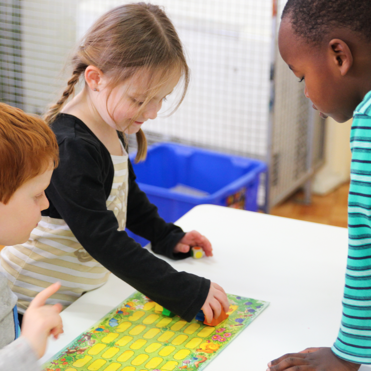 Three students, one girl and two boys, playing a board game at Anglicare's Orana preschool.