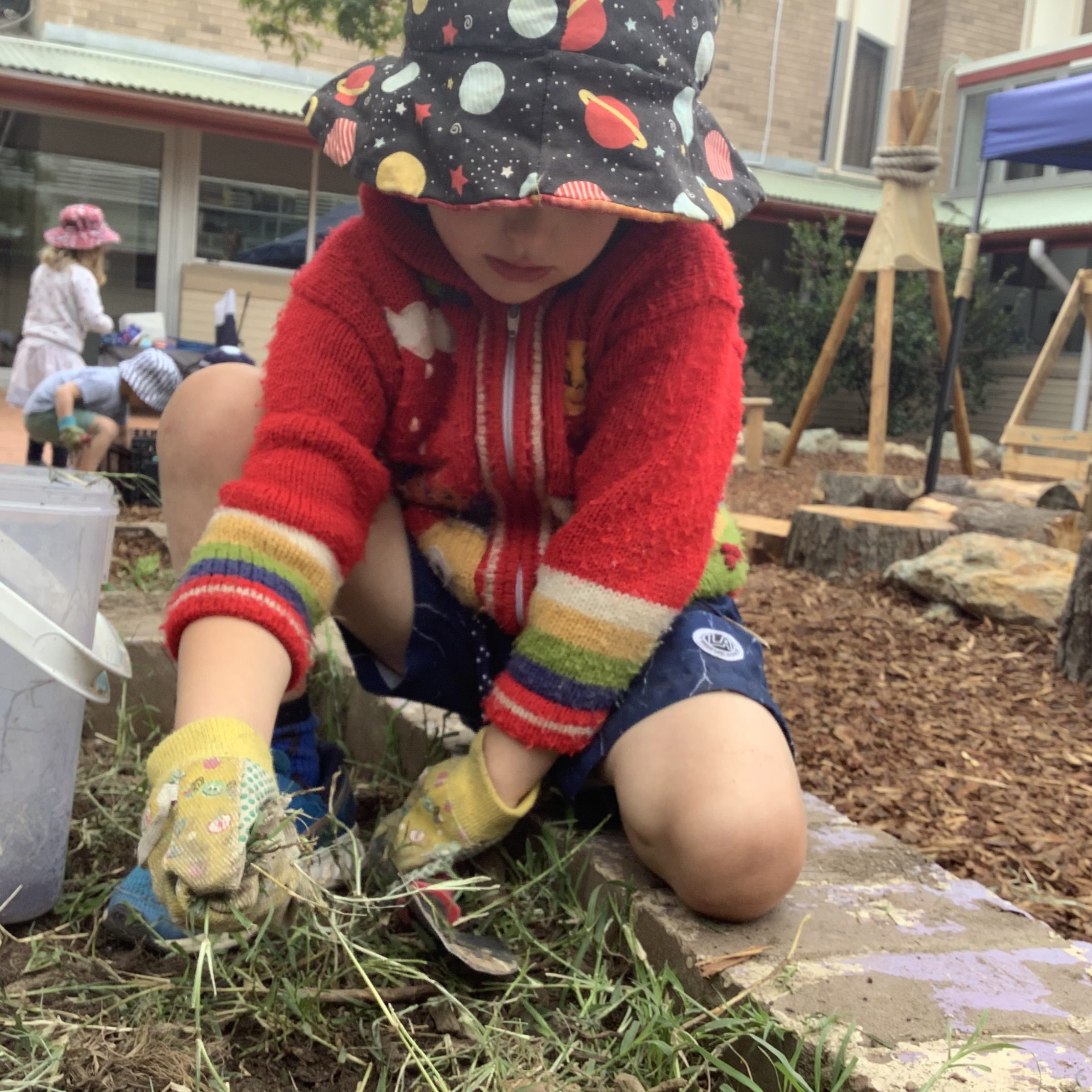 Child wearing gardening gloves and playing in the garden at Anglicare at Southern Cross ELC