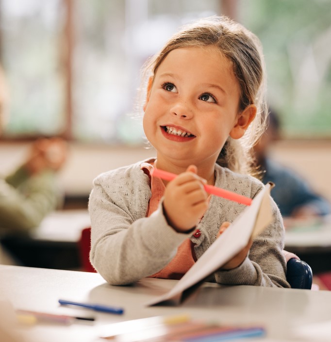 girl sitting at a desk using her pen to show her teacher her artwork