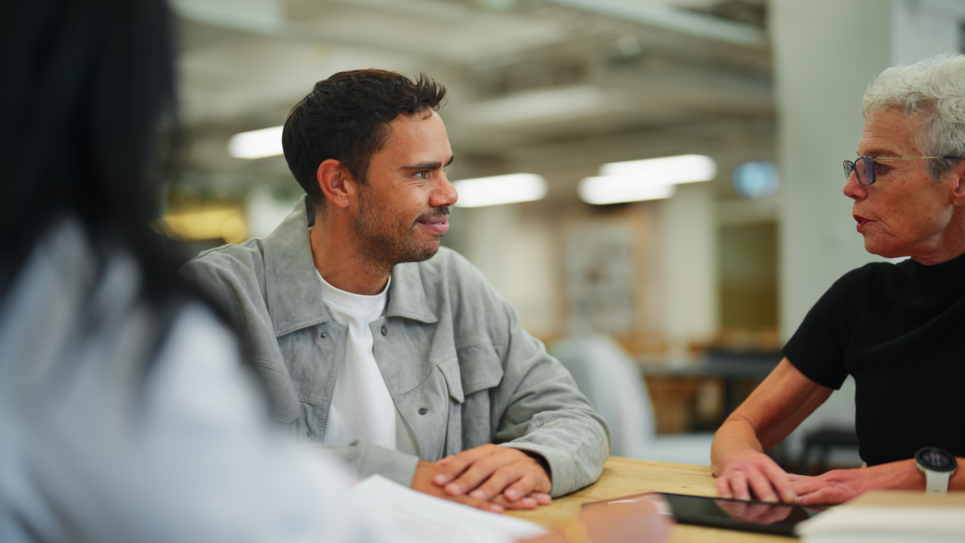 Man sits at desk with a women who is giving financial counselling services.