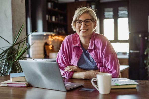 woman sitting at desk with computer, coffee, text book and notebook doing online learning